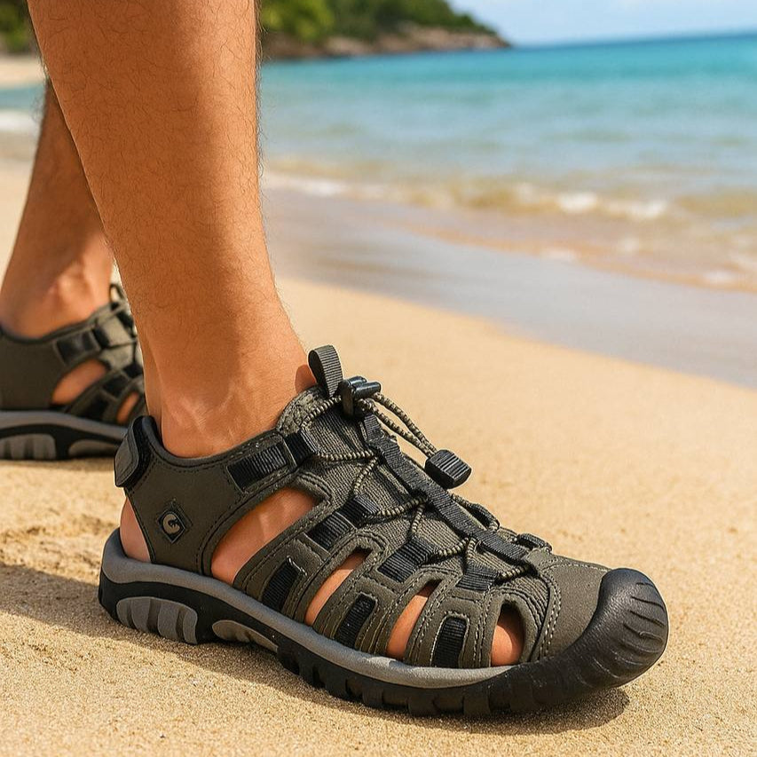 Person wearing black sandals on a beach with ocean and sky in the background