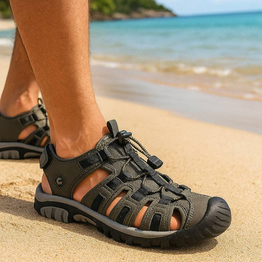 Person wearing black sandals on a beach with ocean and sky in the background
